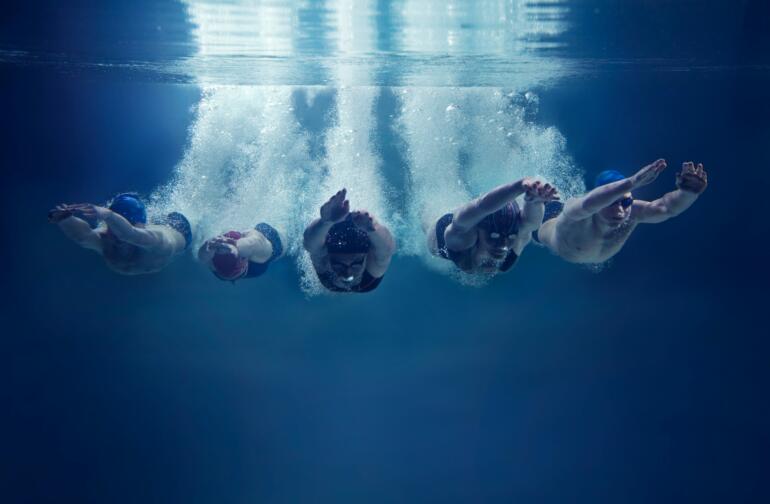 Five swimmers jumping together into water, underwater view